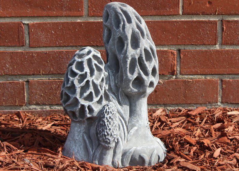 Gray mushroom-shaped garden sculpture beside a brick wall