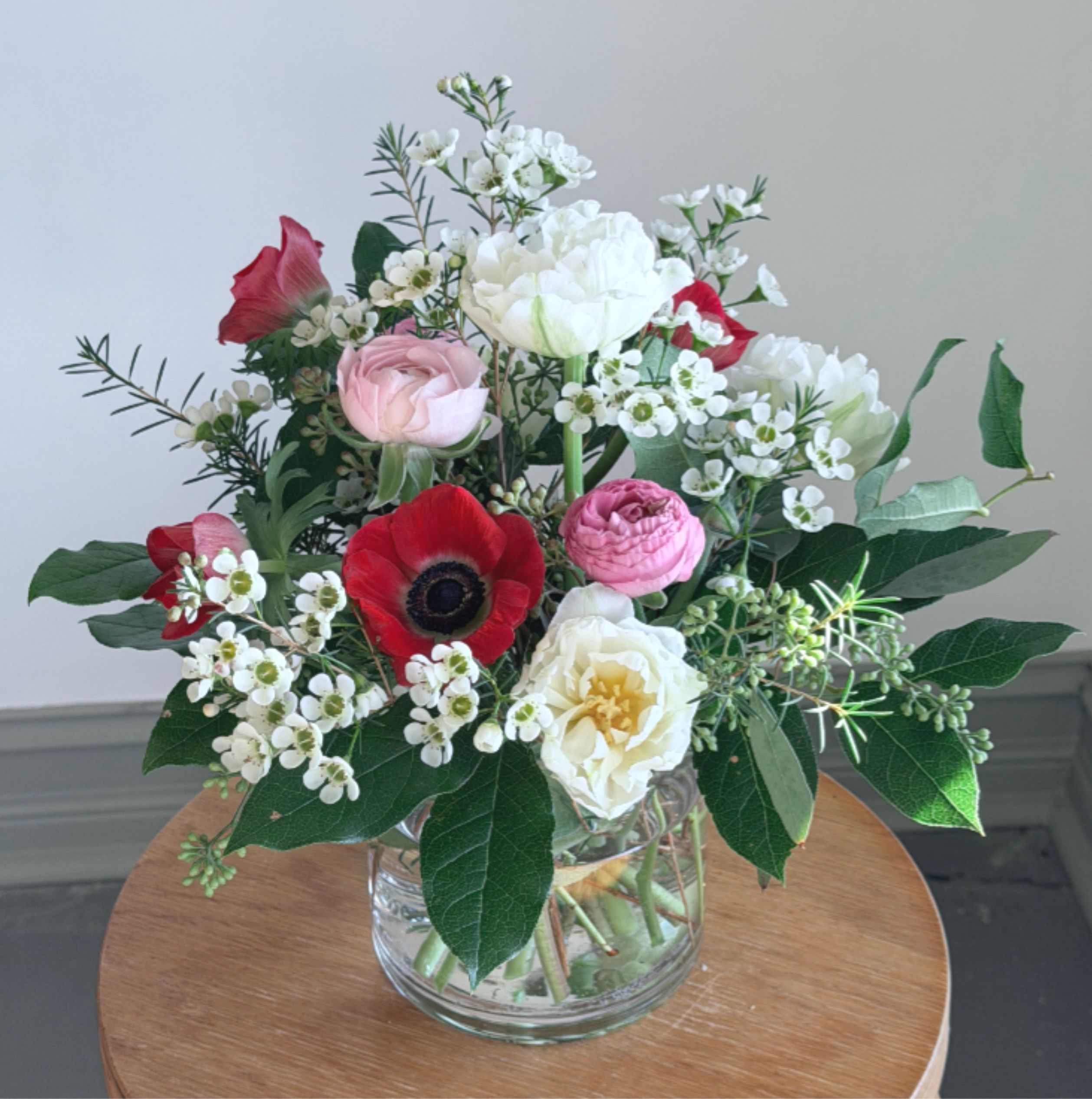 Mixed arrangement of red, pink, and white flowers in a clear glass vase on a wooden table