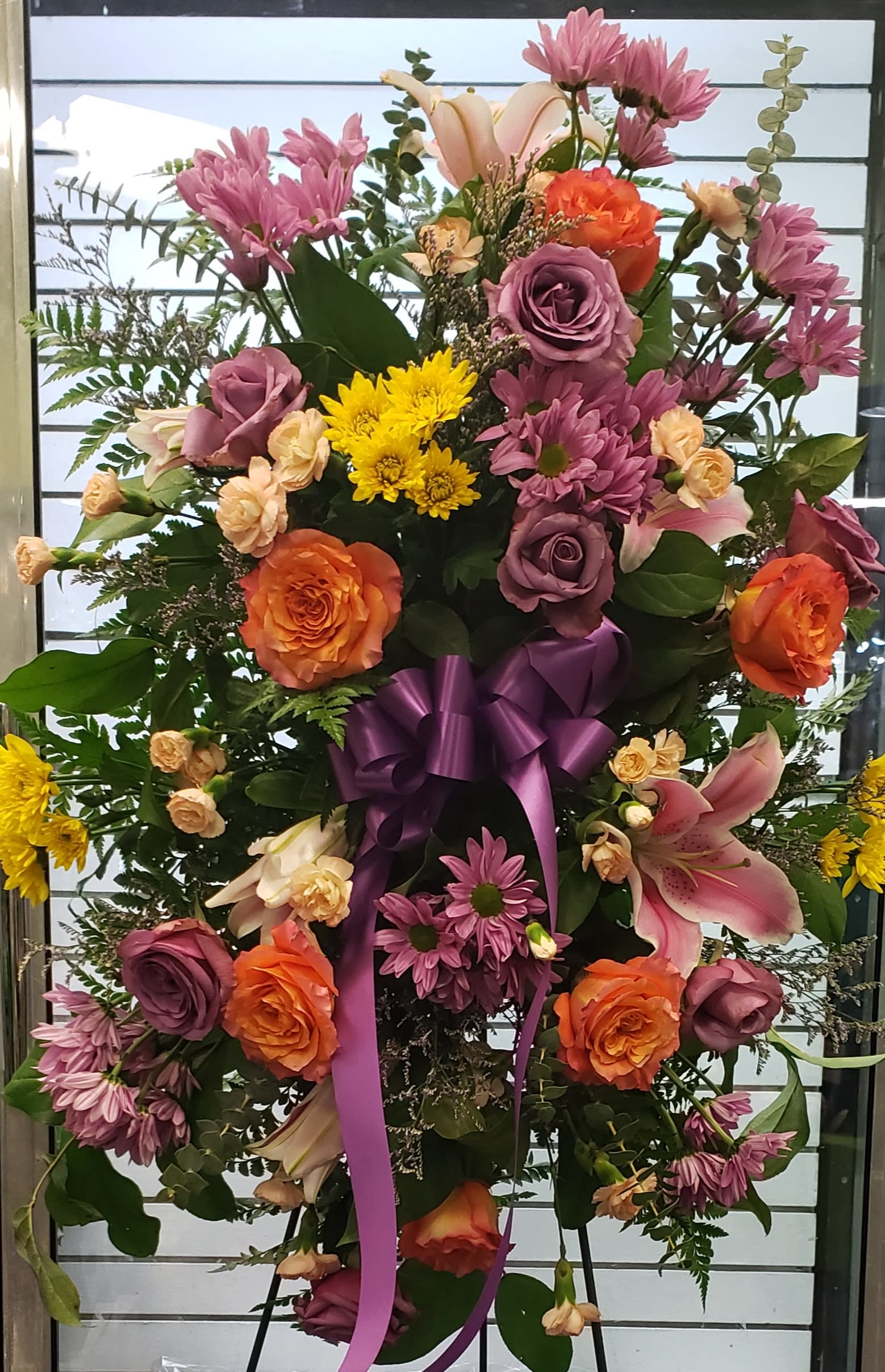 Large standing floral spray with roses, lilies, and chrysanthemums tied with a purple ribbon