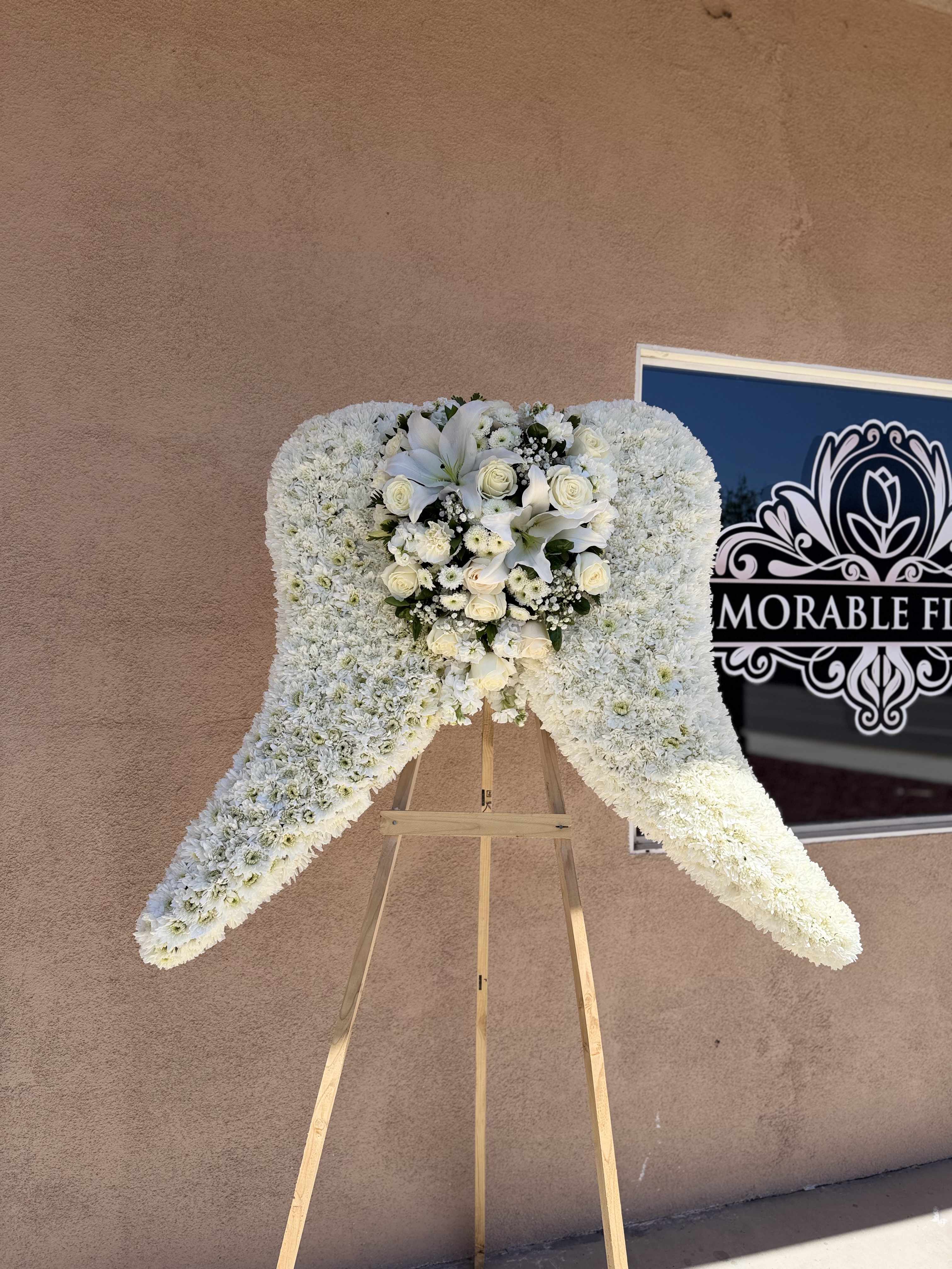 White floral standing spray on a wooden easel with roses and lilies