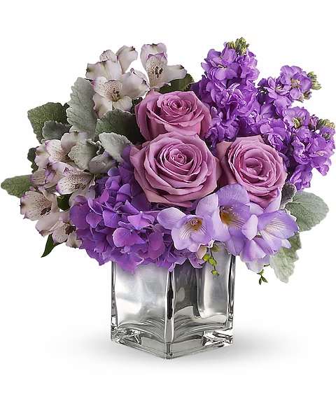 Purple roses and mixed lavender flowers in a clear square vase