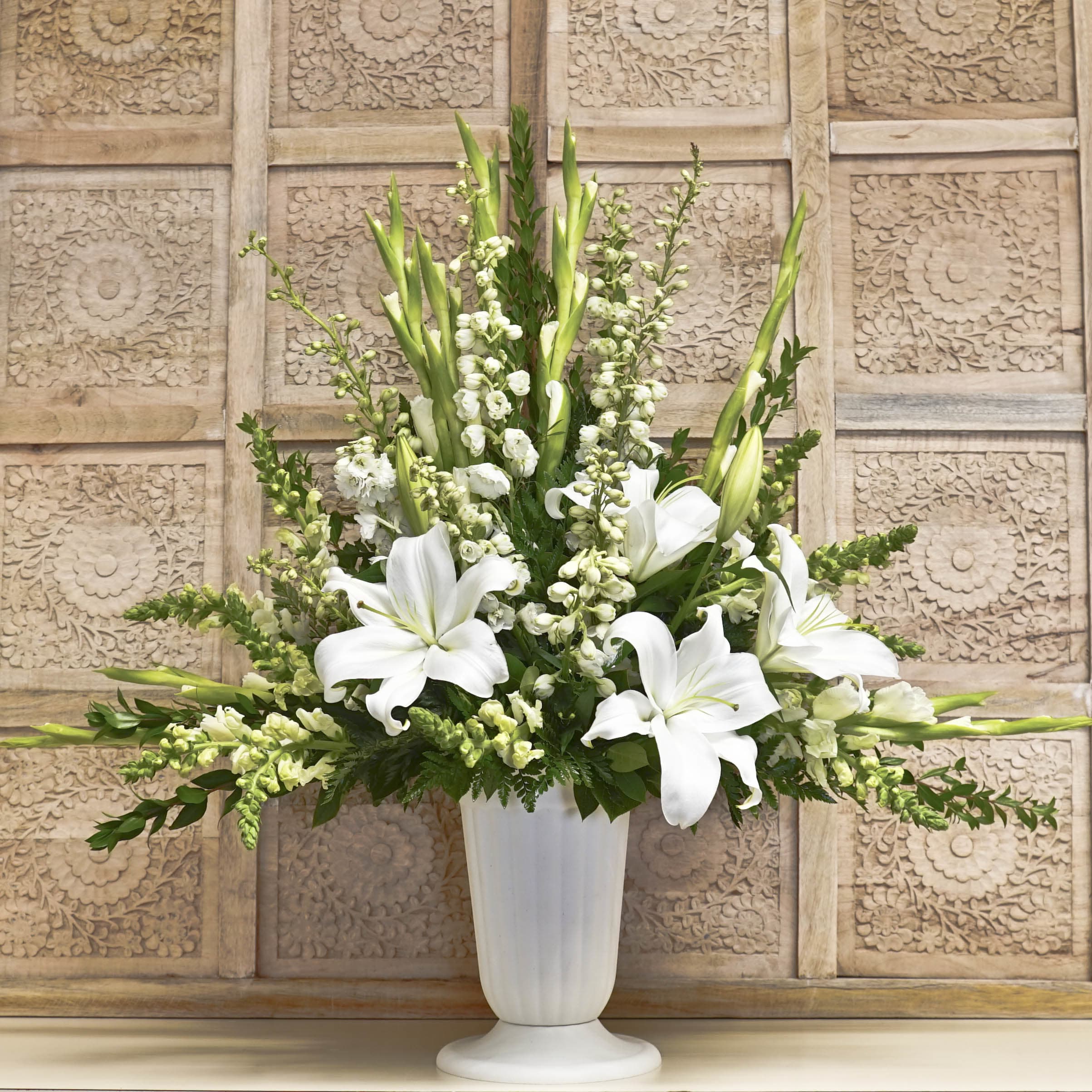 White lilies and tall white blooms arranged in a white pedestal vase