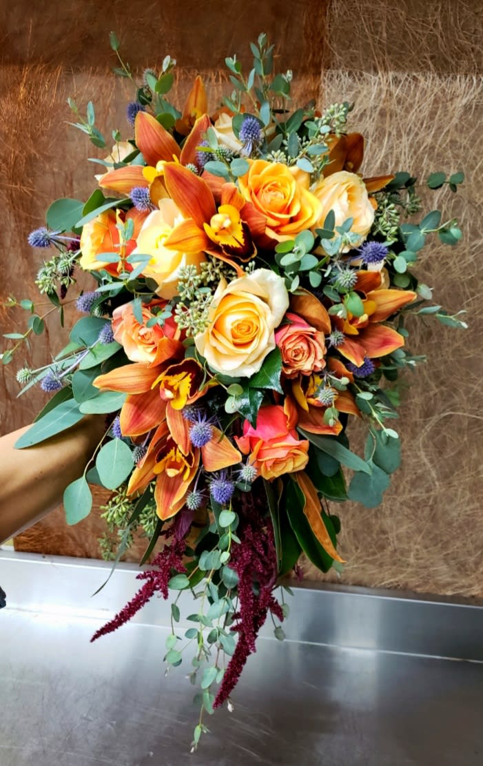 Bouquet of orange and cream roses with orange orchids and blue thistle