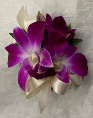 Purple orchid corsage with cream ribbon on a light fabric background