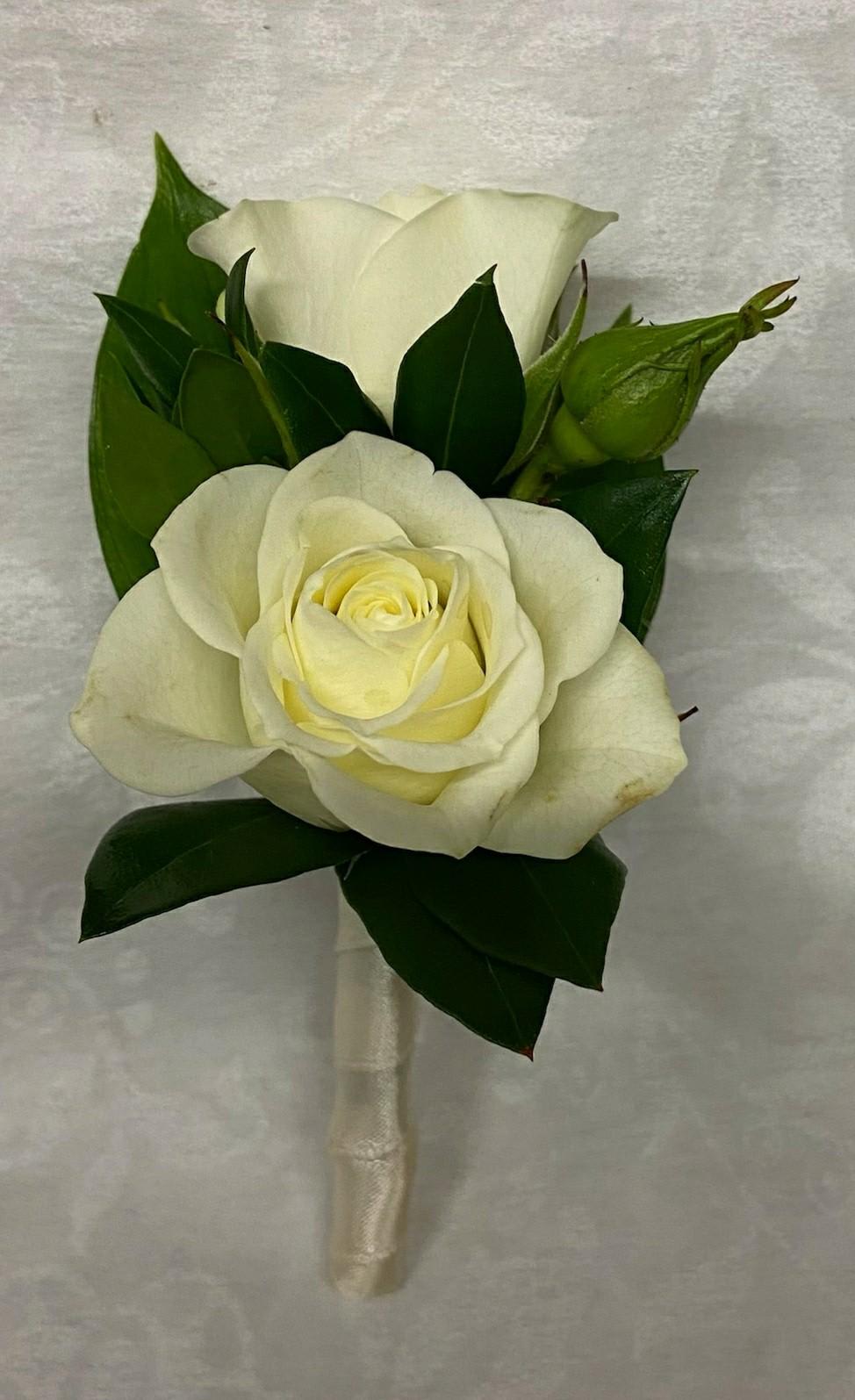 White rose boutonniere with dark green leaves and satin ribbon