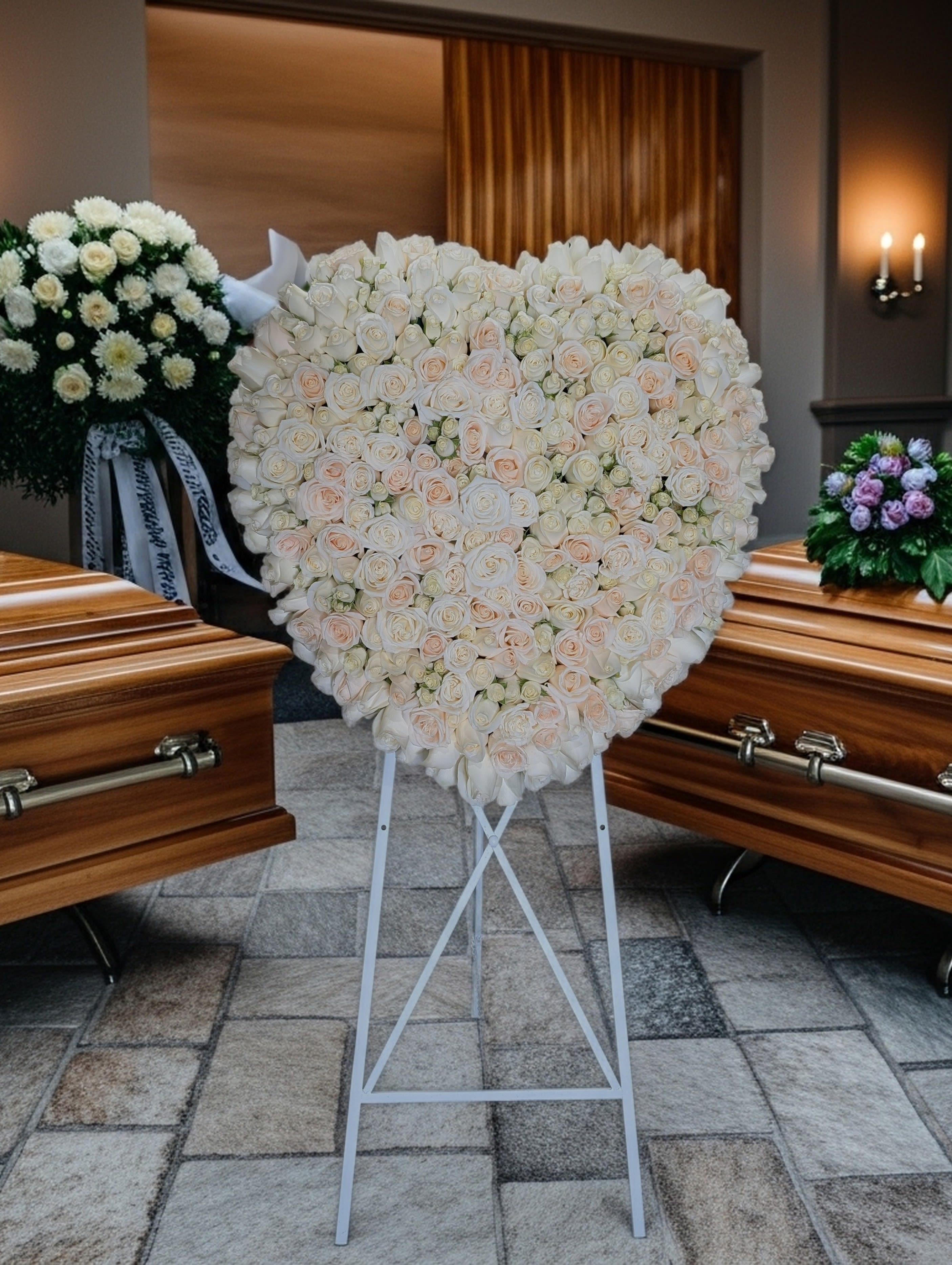 Heart-shaped white rose funeral spray on a stand
