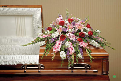 Floral casket spray with pink lilies, red roses, and white blooms