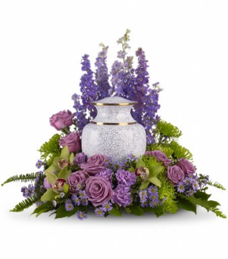 Cremation urn surrounded by purple and green flowers in a low arrangement