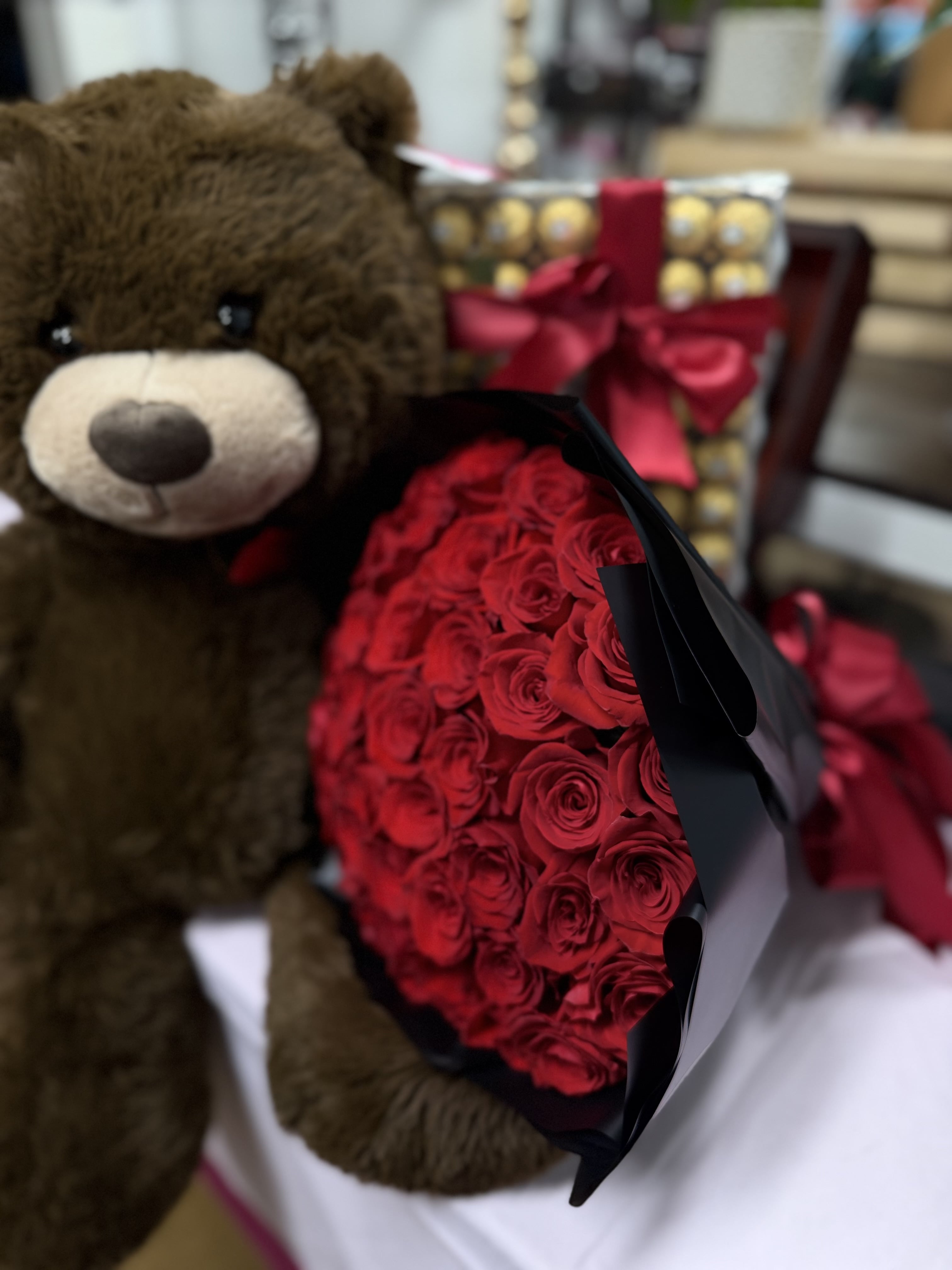 Teddy bear beside a bouquet of red roses and a gift box with a ribbon