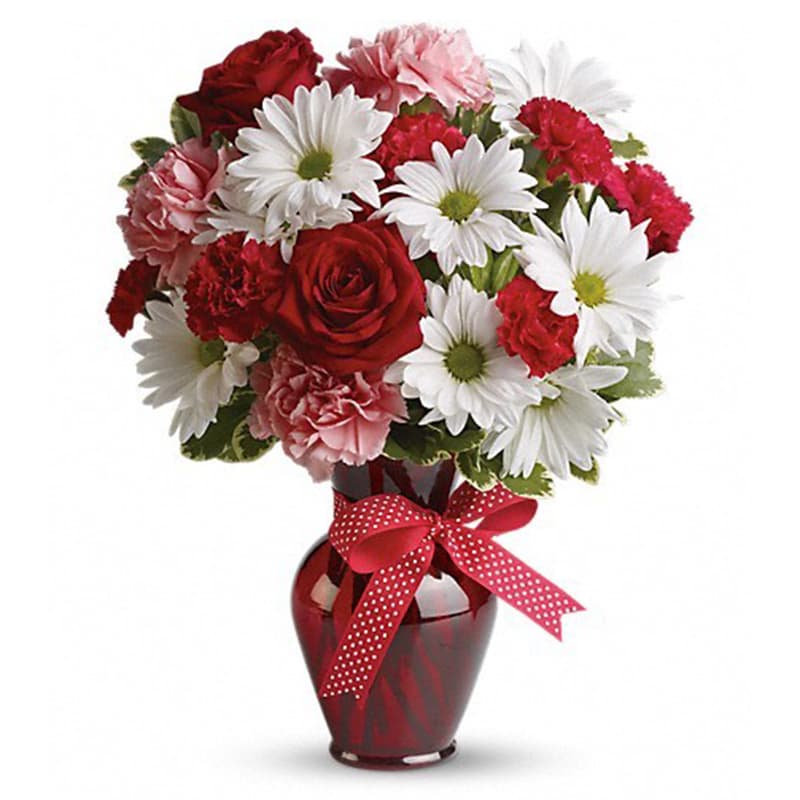 Red and pink flowers arranged in a red vase with a polka-dot ribbon