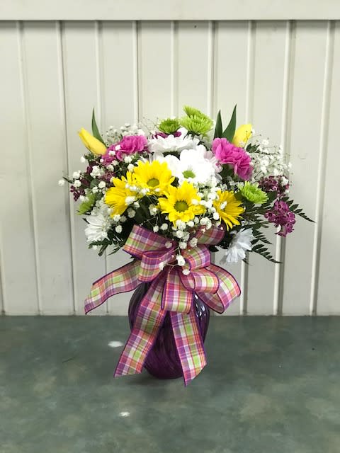 Colorful mixed flower arrangement in a purple vase with a plaid ribbon