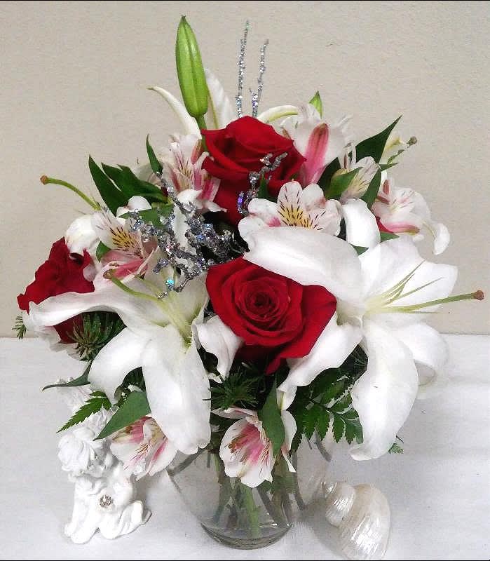 Red roses and white lilies in a clear glass vase with silver accents