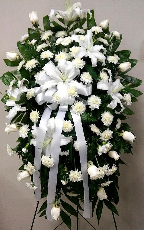 White funeral spray with lilies, mums, and ribbon on an easel