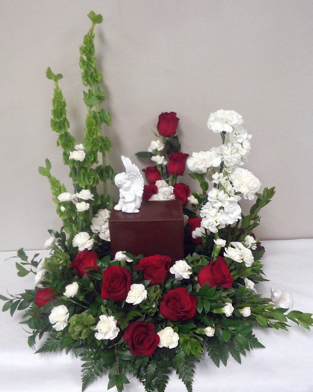 Red roses and white flowers arranged around a small urn with a figurine