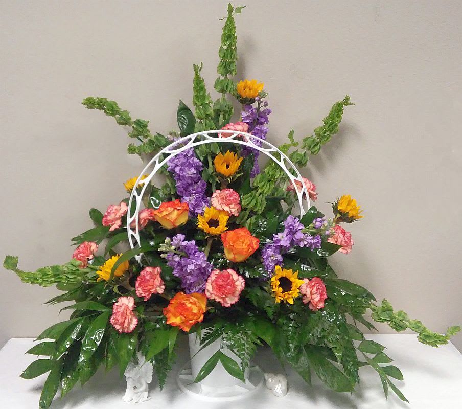 Colorful floral arrangement with sunflowers, roses, carnations, and purple blooms in a white basket