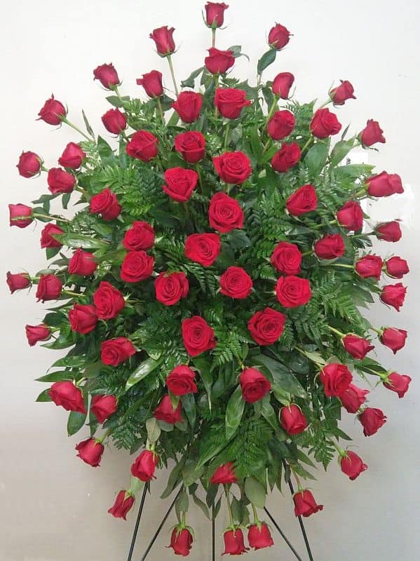 Standing spray of red roses with greenery on a black easel