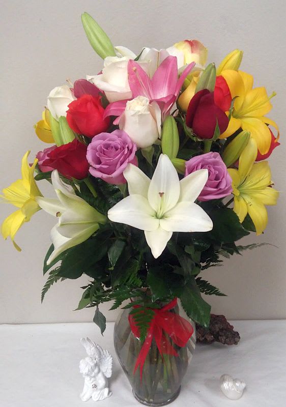 Mixed bouquet of lilies and roses in a glass vase with a red ribbon