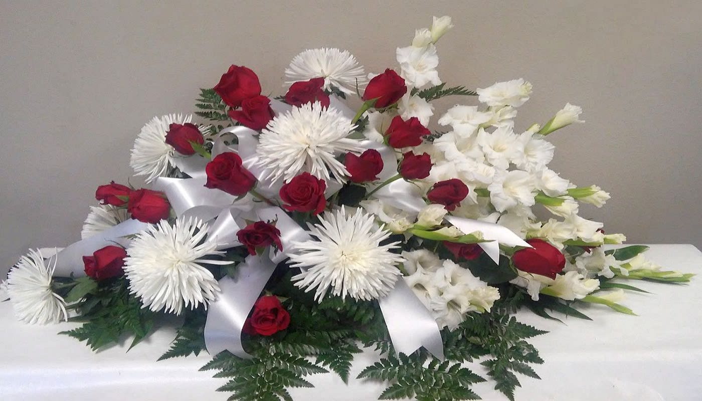 Red roses and white flowers arranged with white ribbon on a table