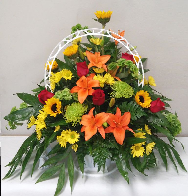 Mixed bouquet with orange lilies, red roses, and yellow daisies in a white basket