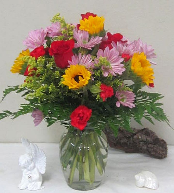 Mixed bouquet of red roses, pink daisies, and yellow flowers in a glass vase