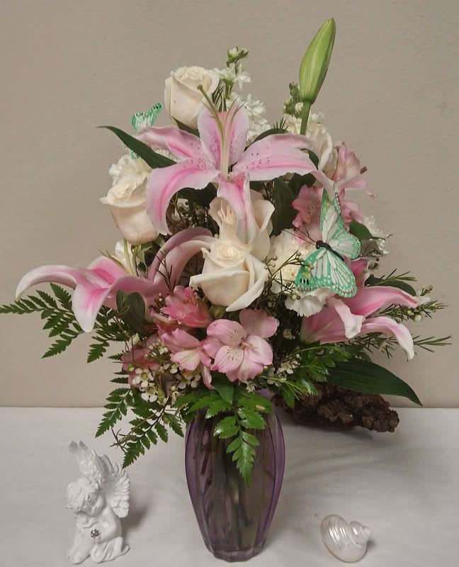 Pink lilies and white roses arranged in a purple vase with butterfly picks