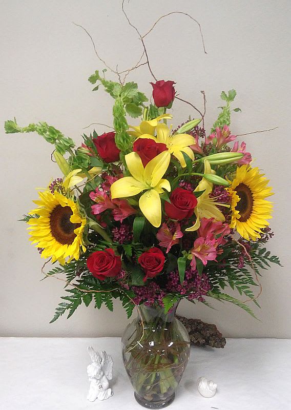 Mixed bouquet with red roses, yellow lilies, and sunflowers in a glass vase