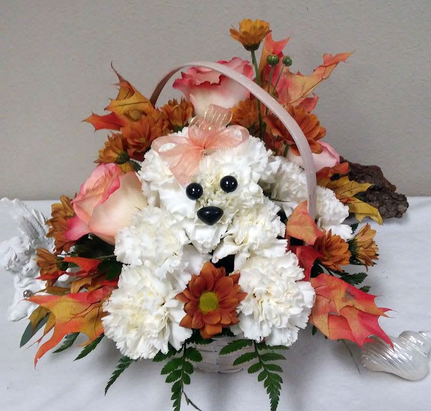 Basket arrangement with white flowers, orange blooms, and a teddy bear face