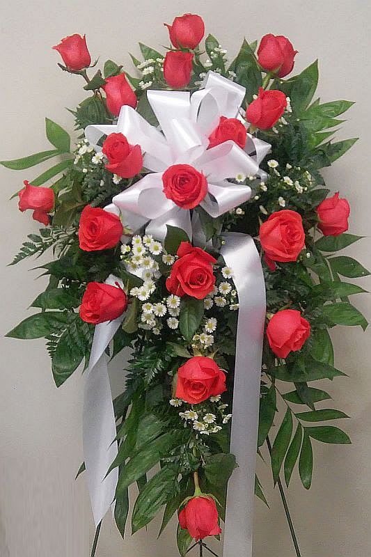 Standing spray of red roses with white ribbon and small white filler flowers