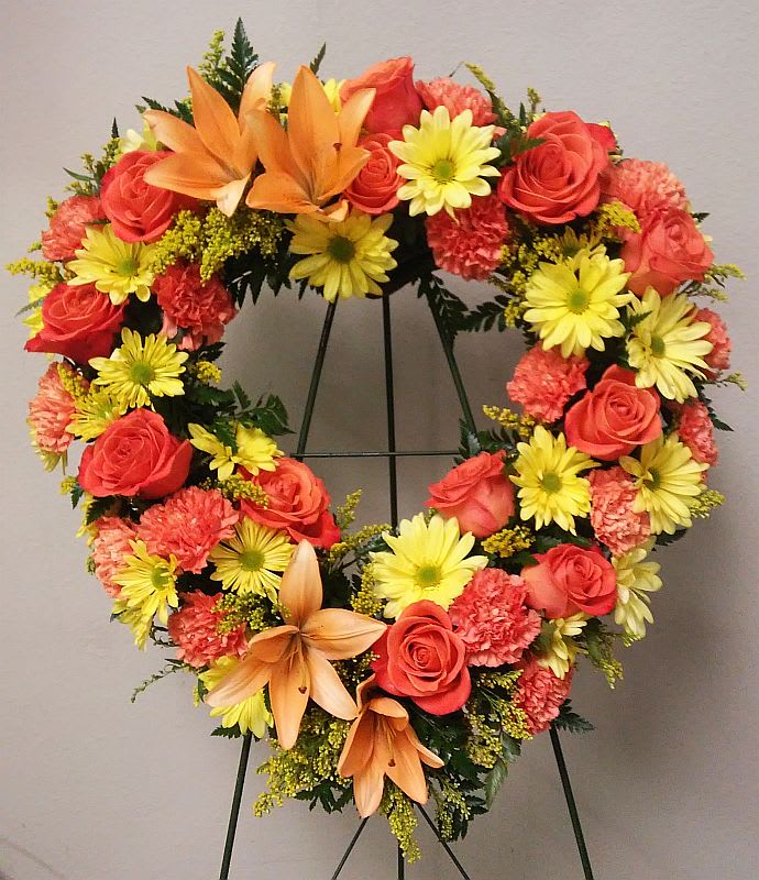Heart-shaped floral wreath with roses, daisies, carnations, and lilies on a stand