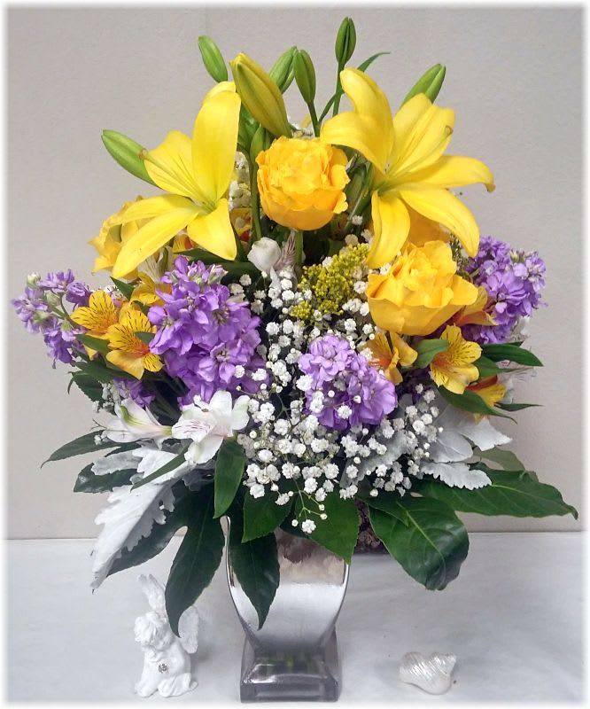 Yellow lilies and purple flowers in a silver vase