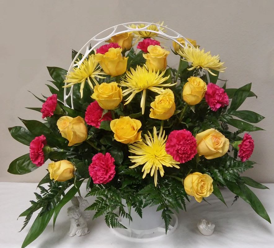 Yellow roses, pink carnations, and yellow spider mums in a white basket arrangement