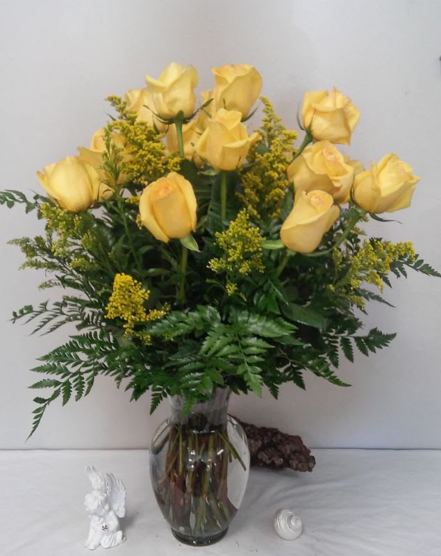 Yellow roses arranged in a clear glass vase with greenery