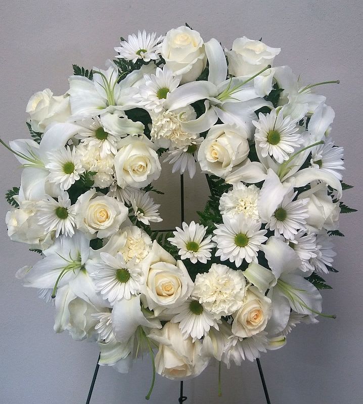 White floral wreath with roses, lilies, and daisies on a stand