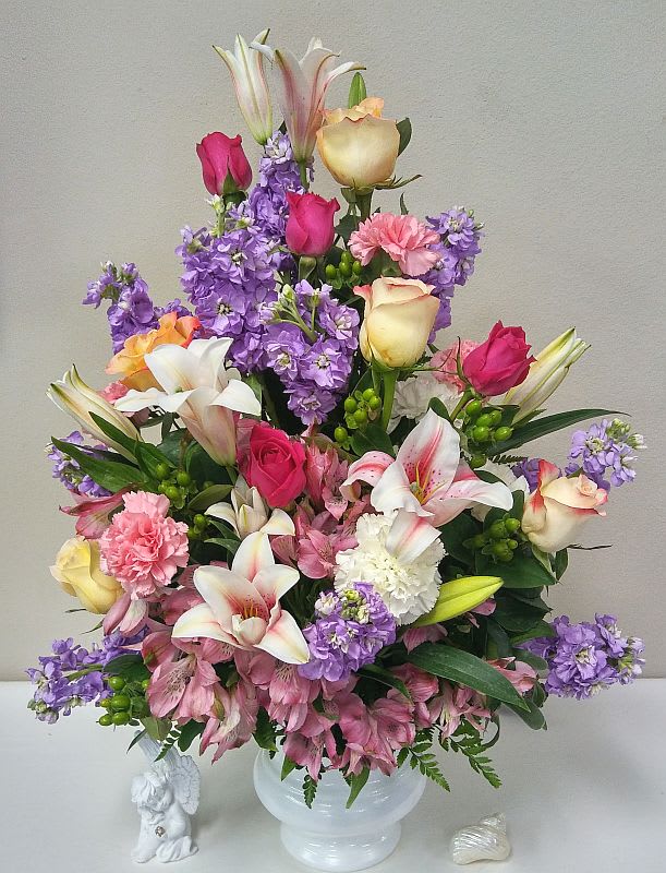 Mixed bouquet of roses, lilies, carnations, and purple flowers in a white vase