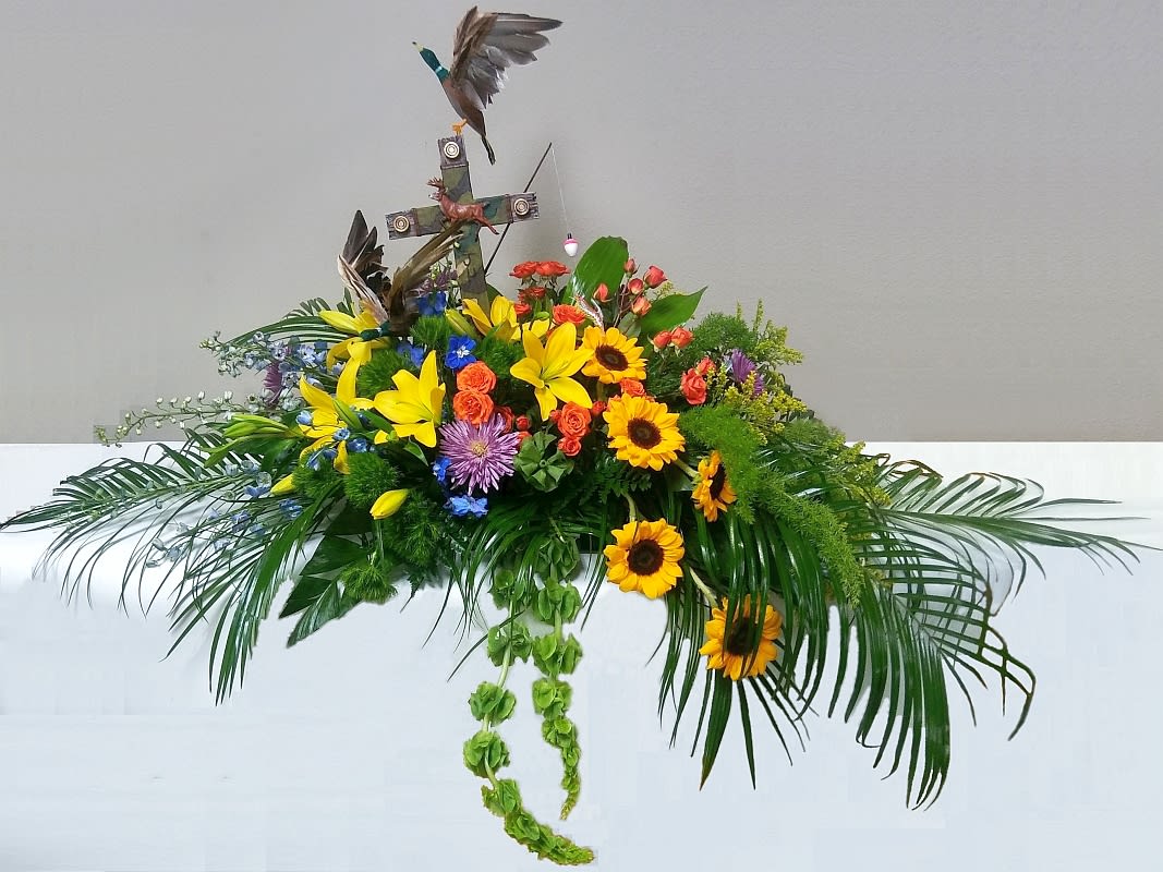 Floral arrangement with sunflowers, lilies, and a cross topper