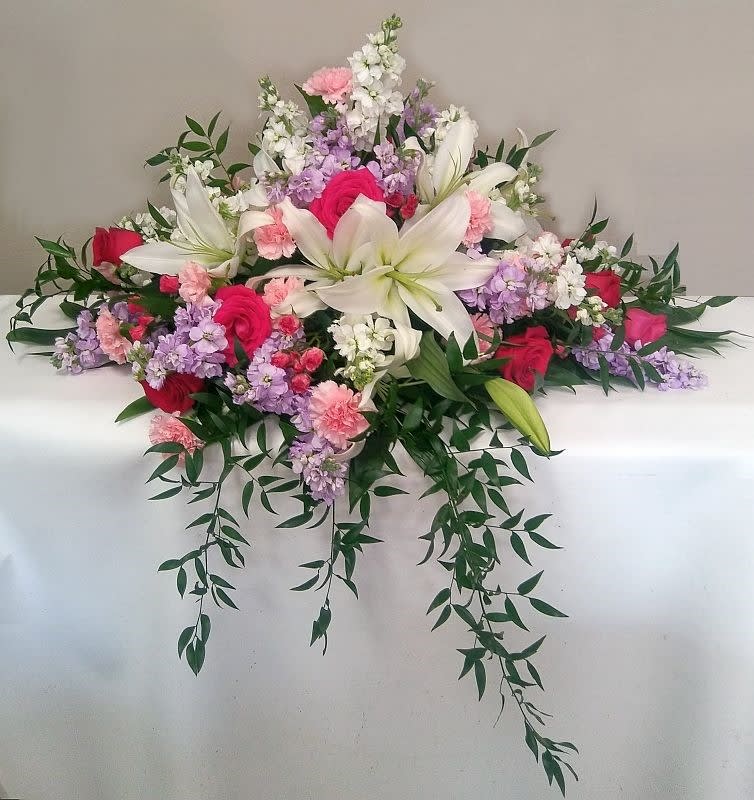 Casket spray with white lilies, pink and purple flowers, and trailing greenery