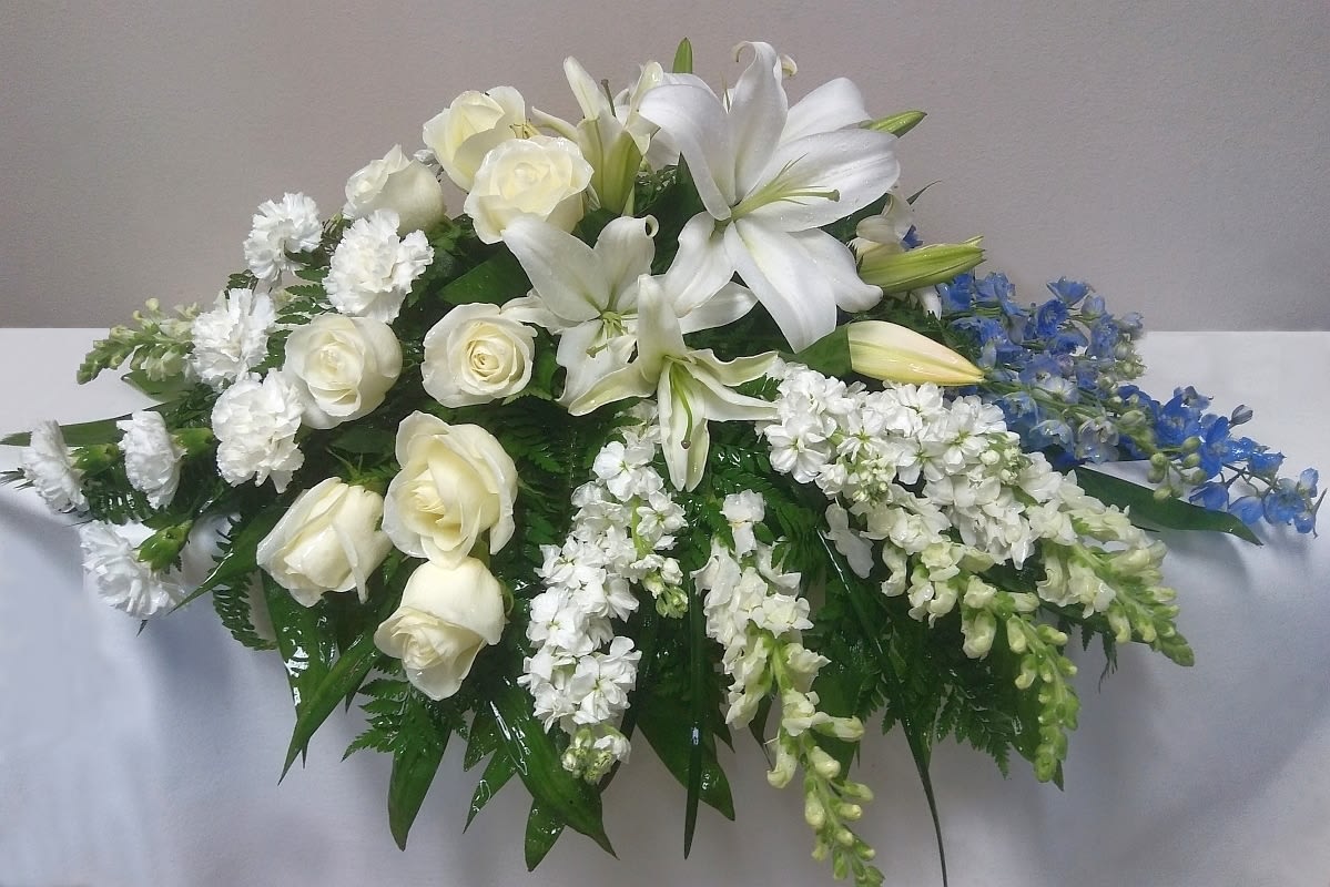 White lilies and roses arranged with blue flowers on a table.