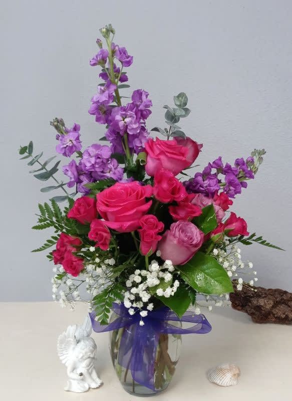 Pink and purple rose bouquet in a glass vase with a purple ribbon