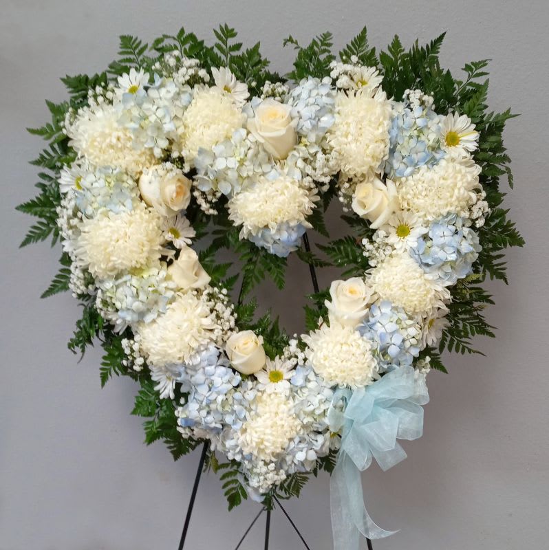 Heart-shaped floral wreath with white and pale blue flowers on an easel
