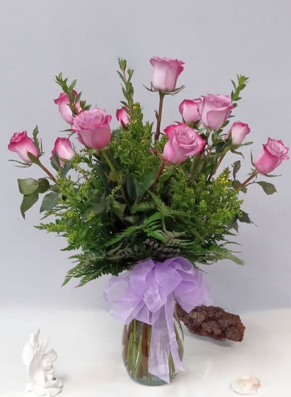 Pink roses in a glass vase with a lavender ribbon bow
