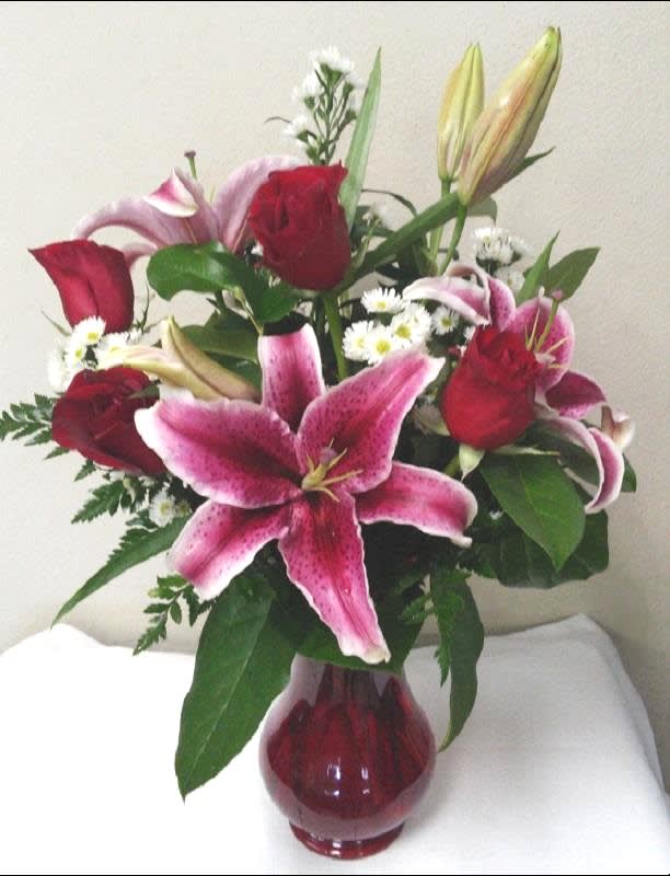 Bouquet of red roses and pink lilies in a red glass vase