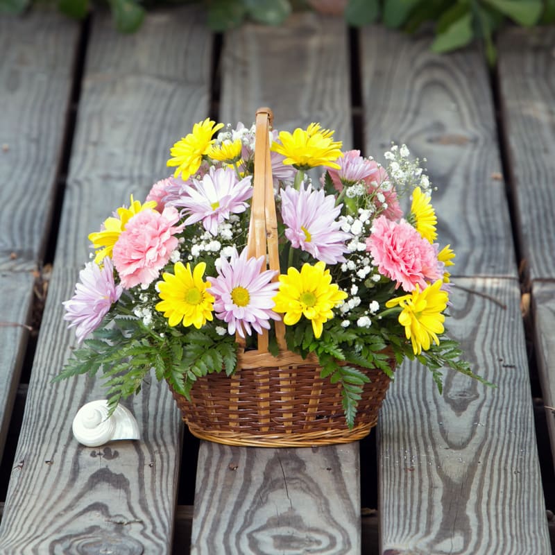 Basket of yellow, pink, and lavender flowers on a wooden deck
