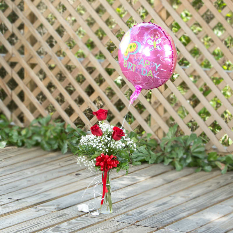 Red roses in a glass vase with a pink birthday balloon