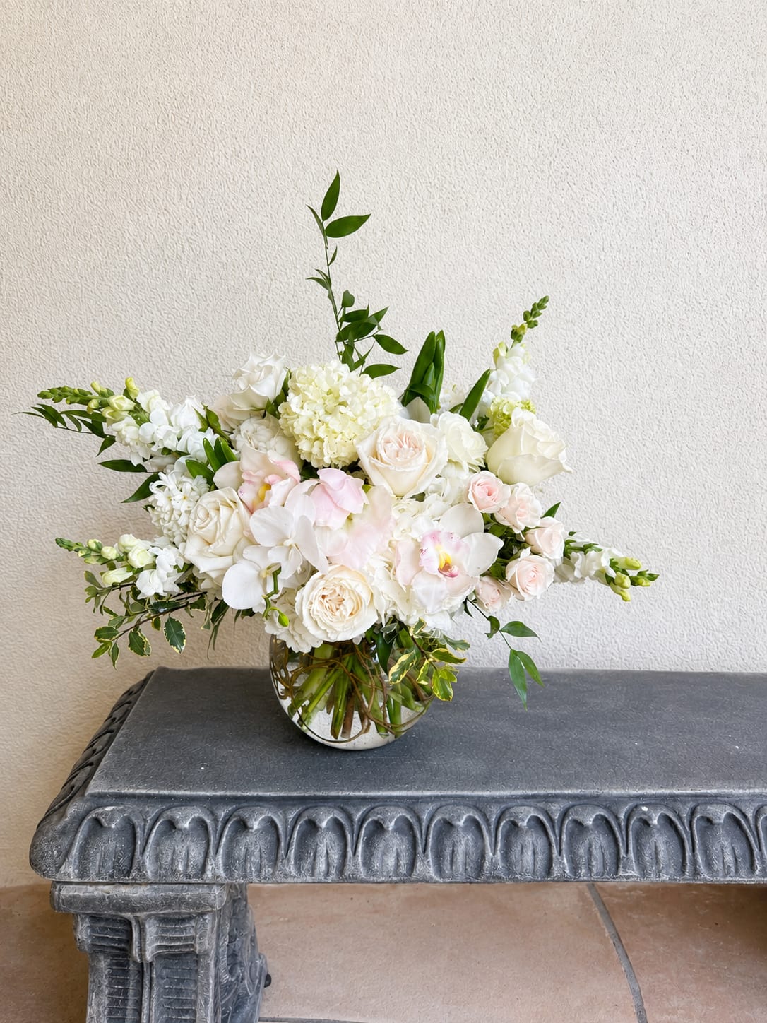 White and blush floral arrangement in a round glass vase