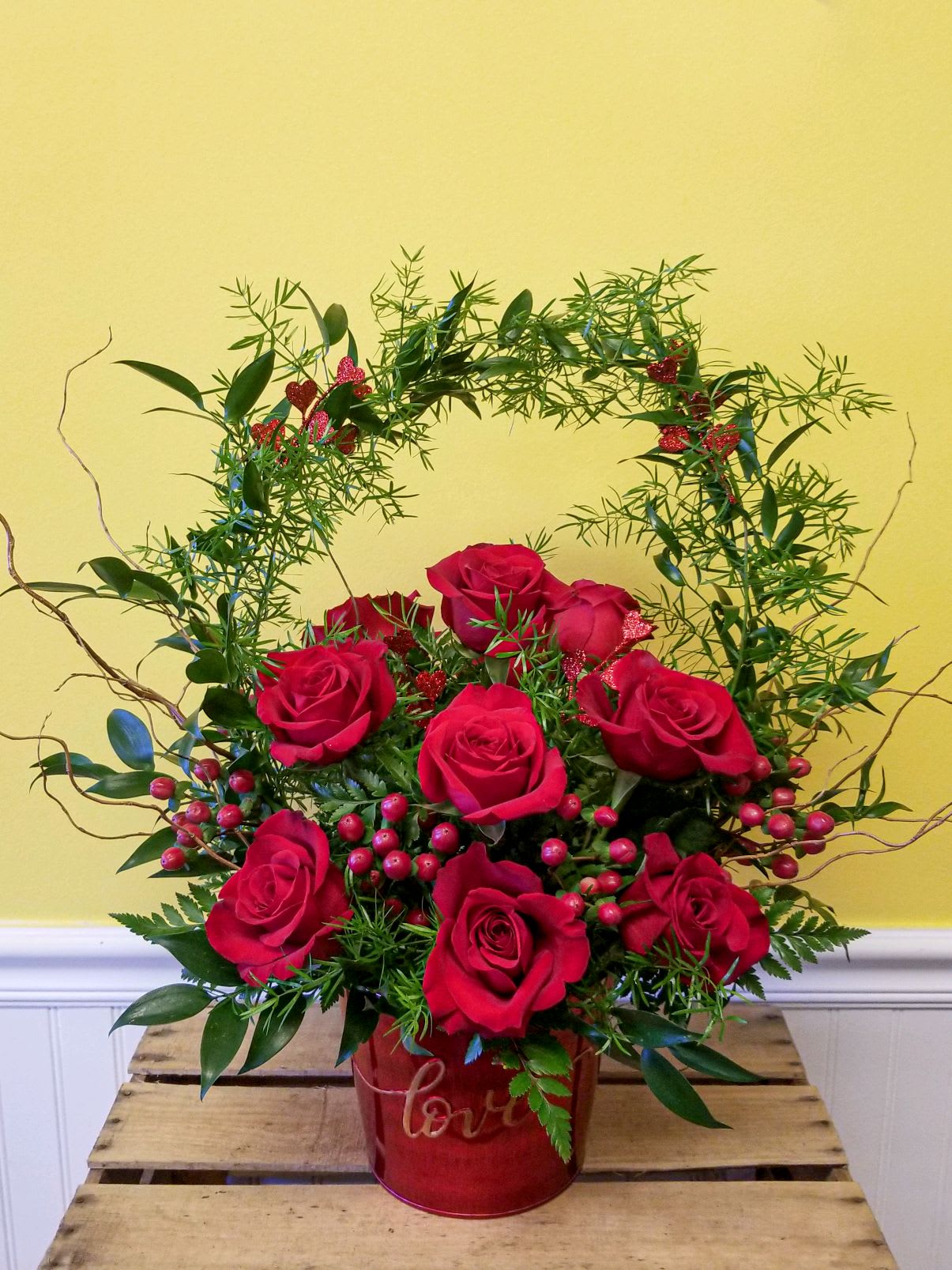 Red roses arranged in a red heart-shaped container with greenery