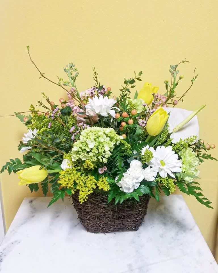 Mixed floral arrangement in a woven basket with yellow tulips and white daisies