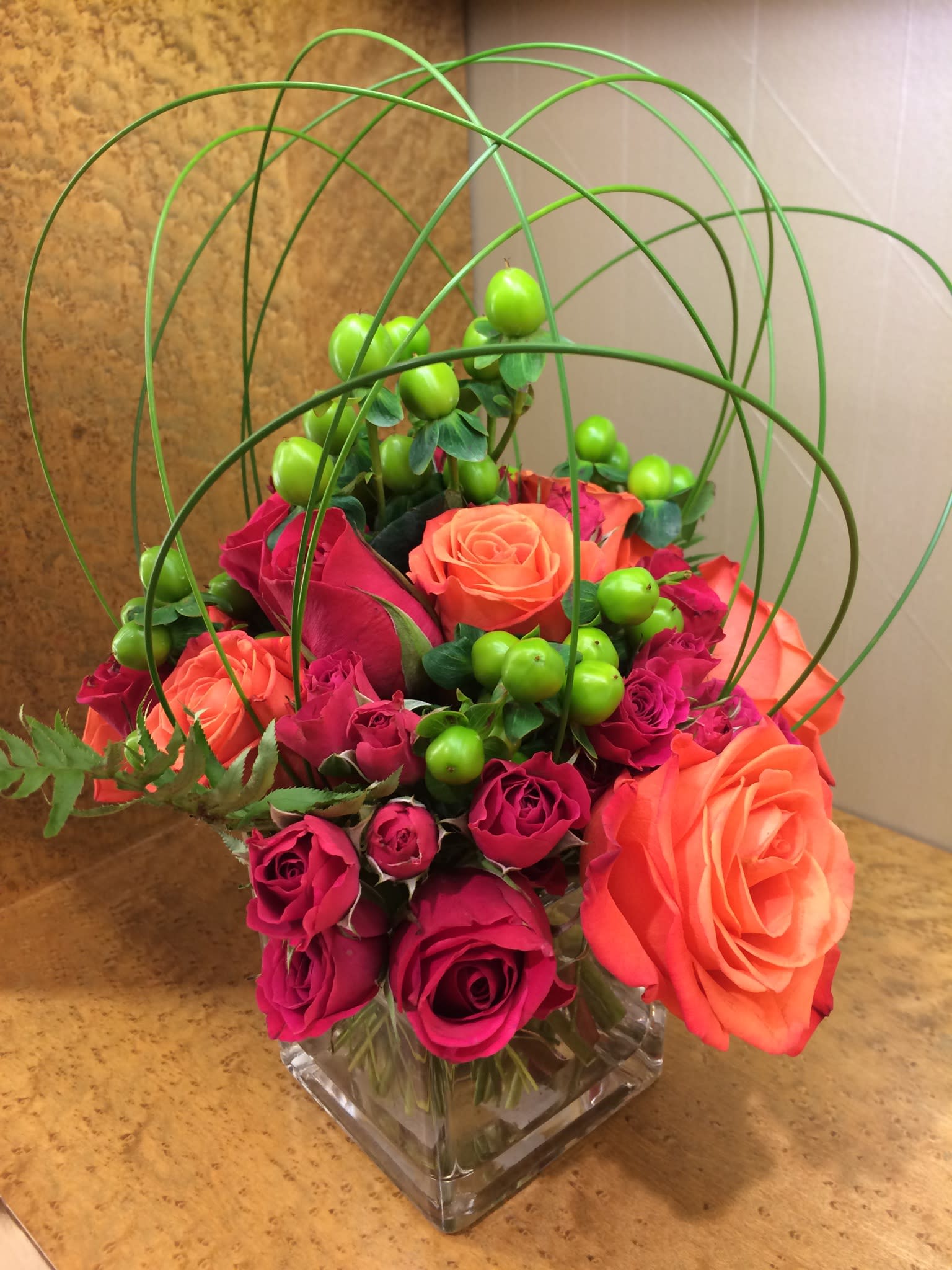 Pink and orange roses in a square glass vase with green berry accents