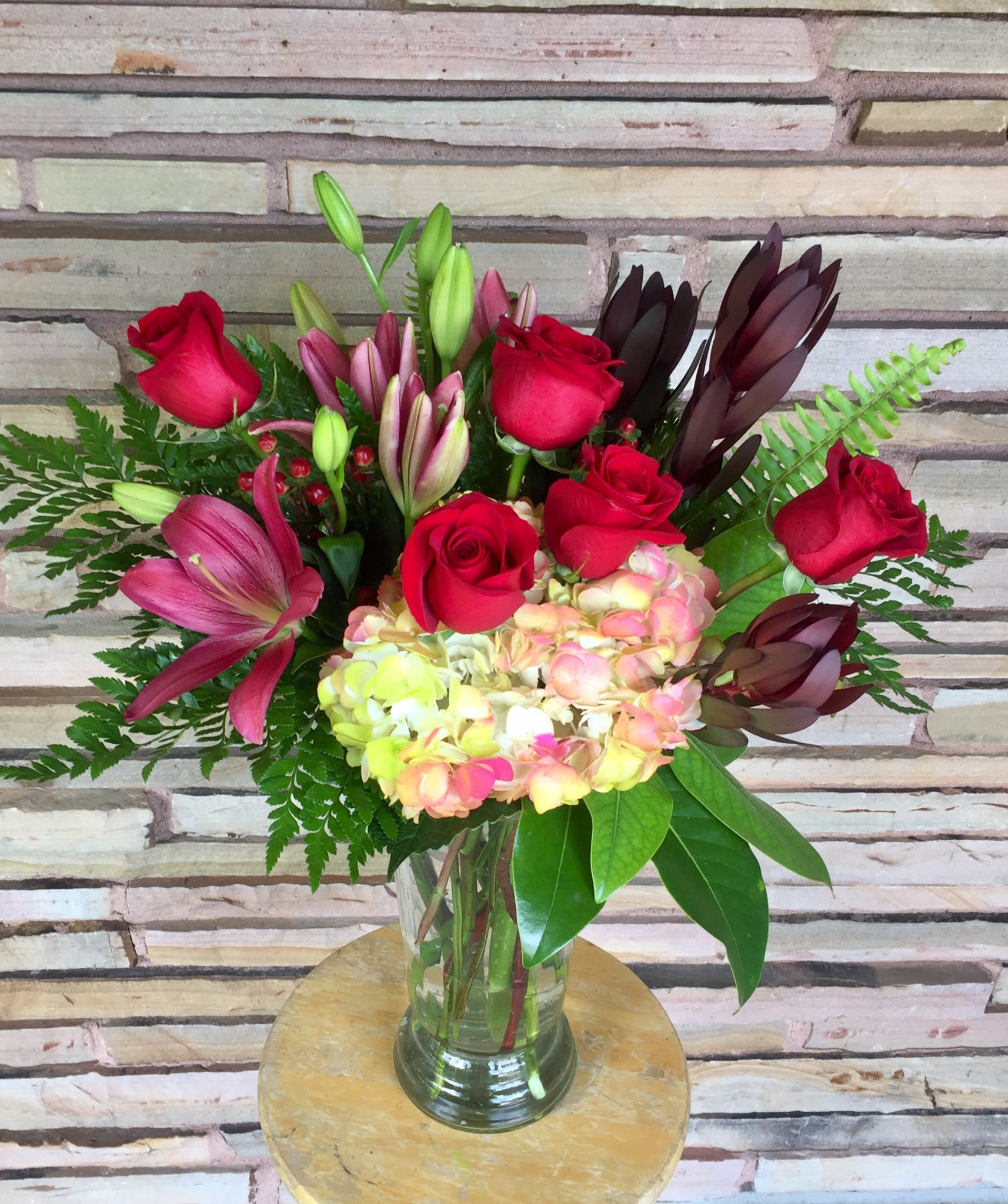 Bouquet of red roses, lilies, and hydrangea in a glass vase