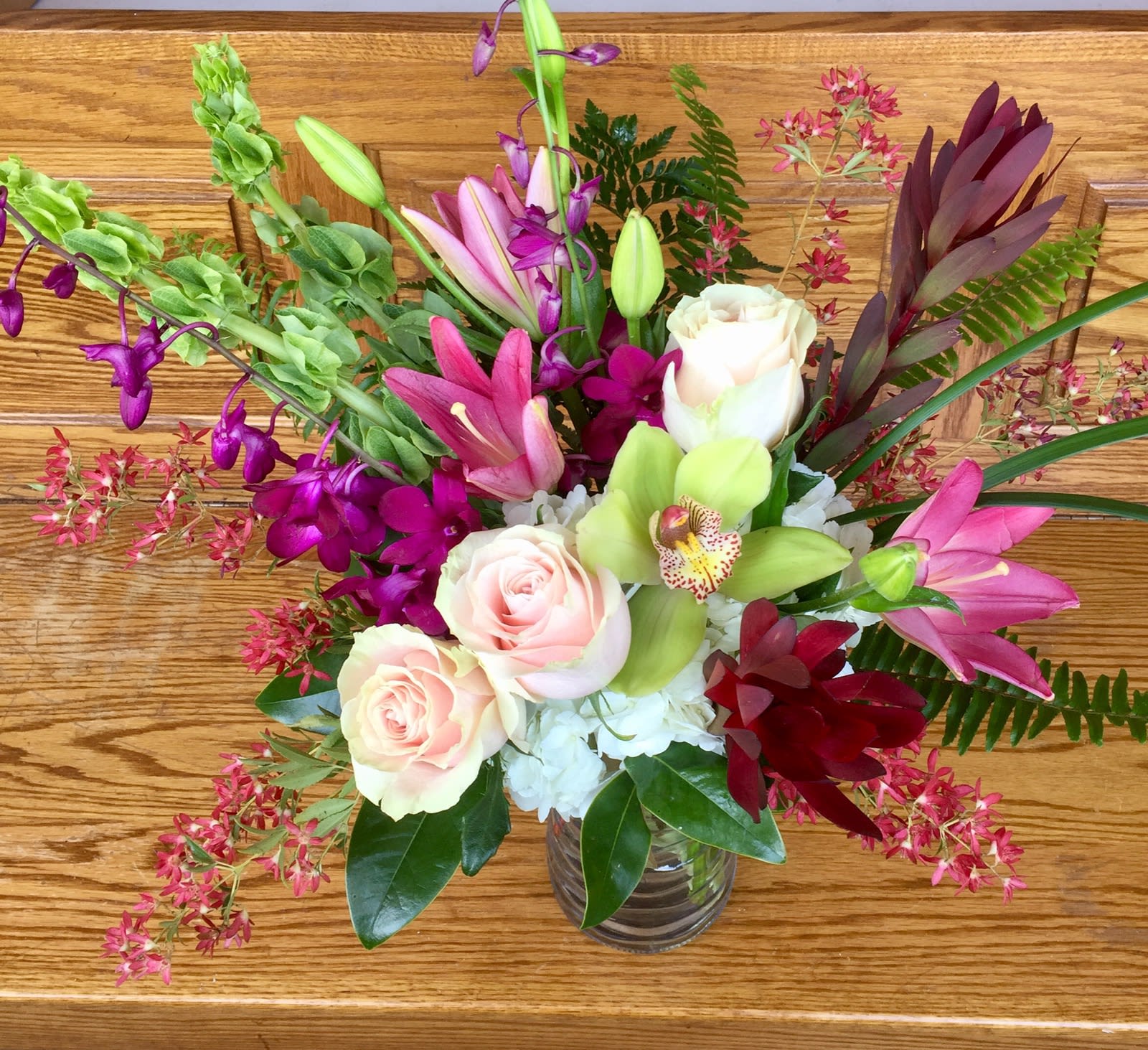 Mixed bouquet of roses, orchids, and lilies in a glass vase