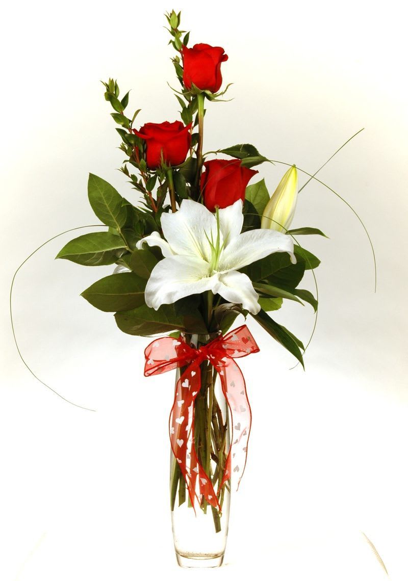 Red roses and a white lily in a clear vase with a red ribbon
